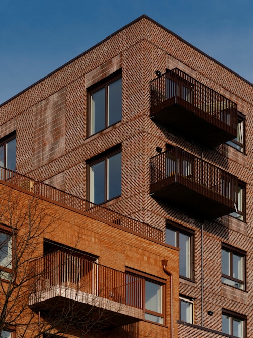 Foto av fasaden på en leilighetsblokk på Nansenløkka på Fornebu. Blokken er bygget i teglstein med svarte gitterbalkonger.
