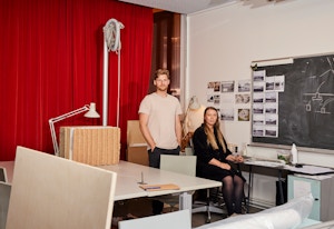 Jonas og Siren i et arbeidsrom på Arkitektur- og design høgskolen i Oslo. Jonas står og Siren sitter ved en pult.