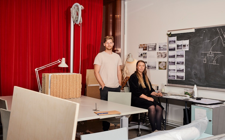 Jonas og Siren i et arbeidsrom på Arkitektur- og design høgskolen i Oslo. Jonas står og Siren sitter ved en pult.