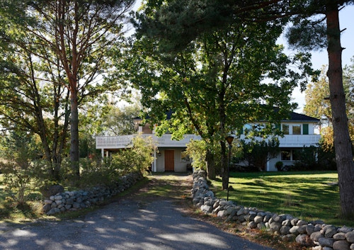 Bildet viser innkjørselen til et hvitt block watne-hus med trær rundt.