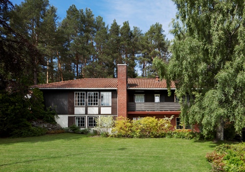 Et block watne-hus pipa plassert midt i huset, og med plen og trær rundt huset.