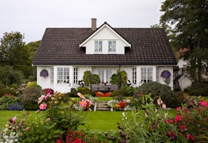 Et hvitt Block Watne-hus med frodig, blomsterrik hage foran.