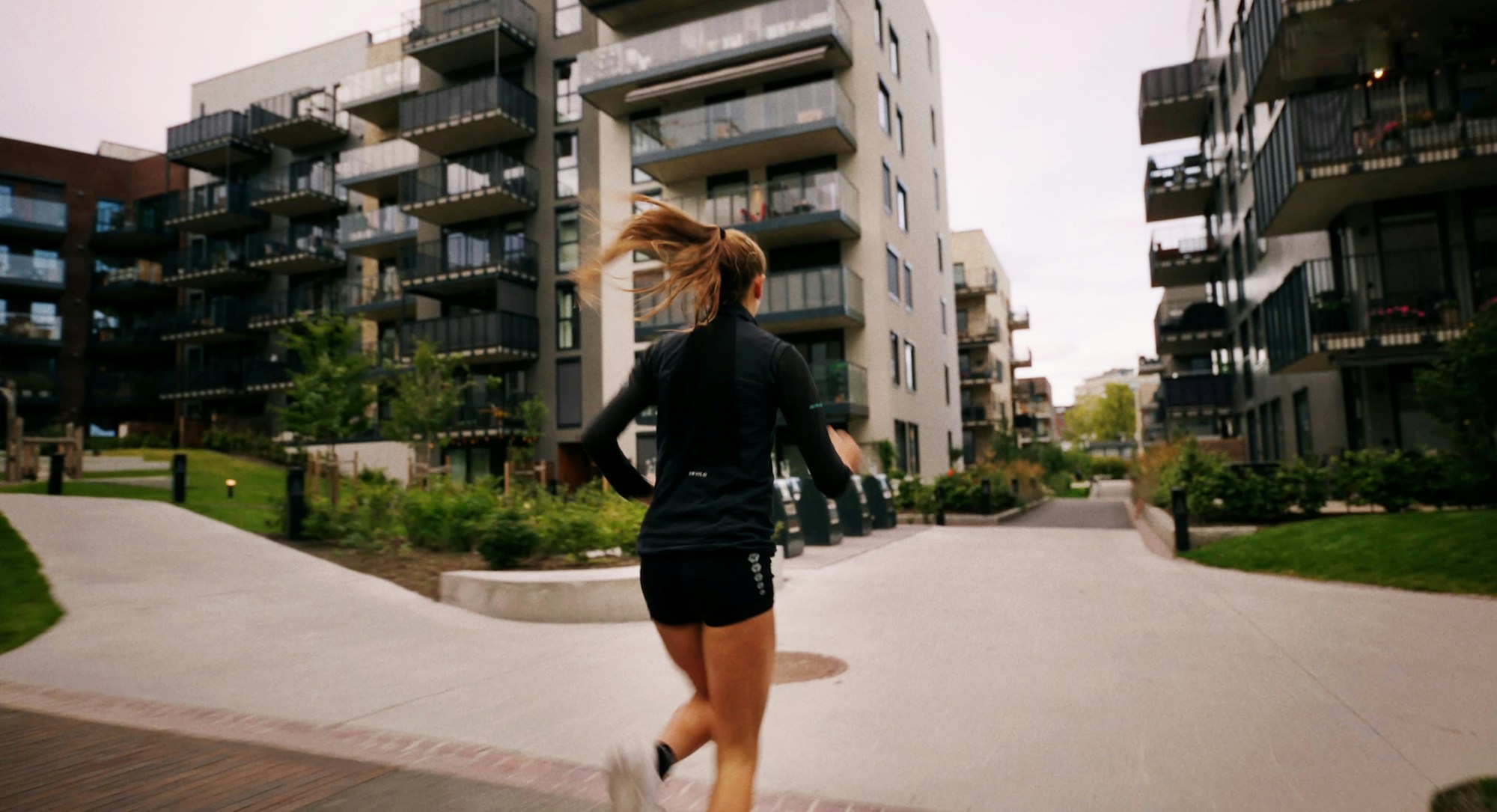 Sigrid løper med ryggen til mellom boligbygg i Frysjaparken.