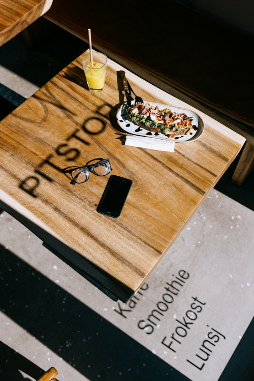 Et kafébord på Pitstop med en lunsjrett og en juice. Tekst fra vinduet med logo og tilbud, kaster en skygge over bordet.