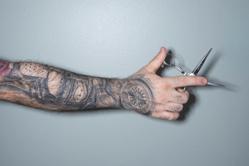 En mannlig tatovert arm holder en frisørsaks