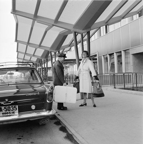 Sort/hvitt bilde av en mann og en kvinne utenfor terminalbygget på Fornebu Lufthavn.