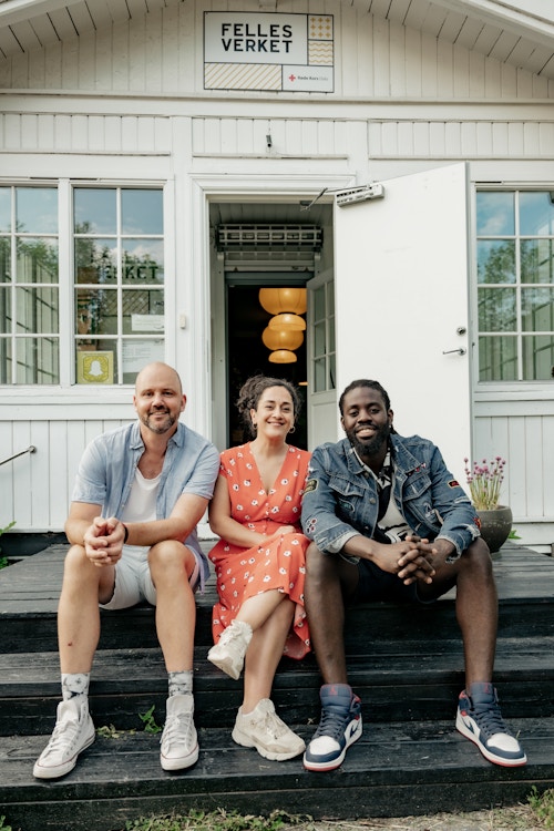 Foto av tre personer som sitter på trappen til hovedhuset til Mortensrud Gård.