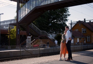 Foto av et par som klemmer på en togstasjon om sommeren.