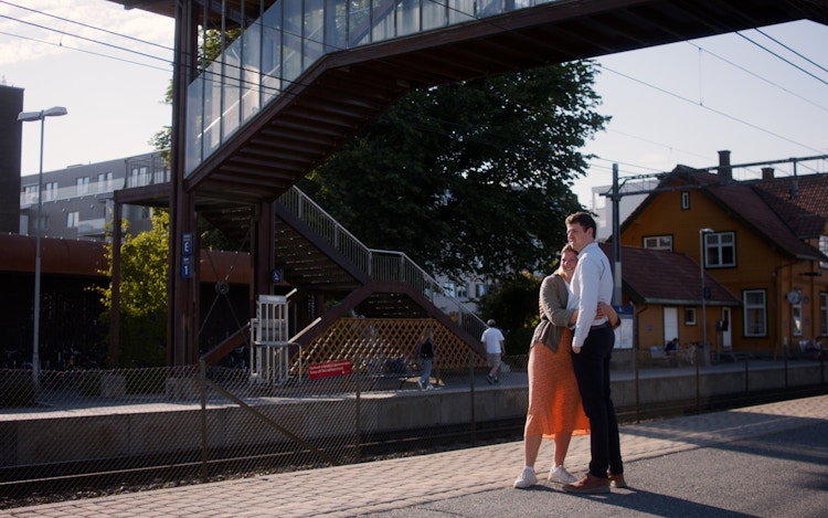 Foto av et par som klemmer på en togstasjon om sommeren.