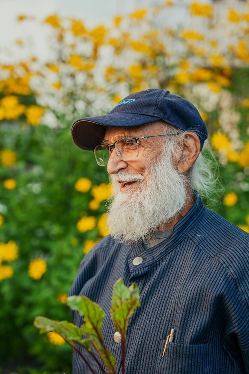 En av naboene i kvarteret, en eldre mann med langt hvitt skjegg smiler blandt blomstene