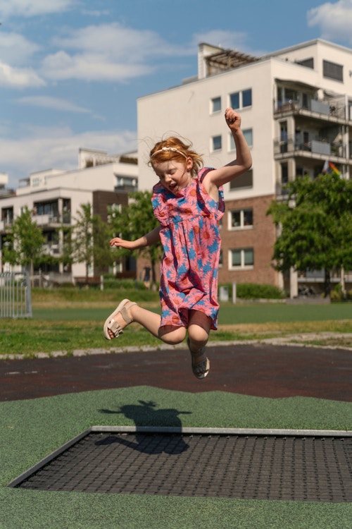 Jente i blomstrete kjole som hopper på en trampoline