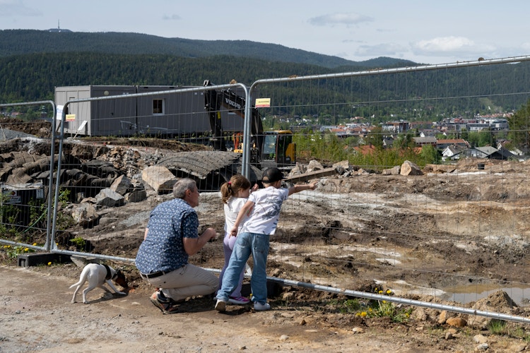 Foto av kjøperen Tor Helge ved byggegjerdet med barnebarna og hunden.