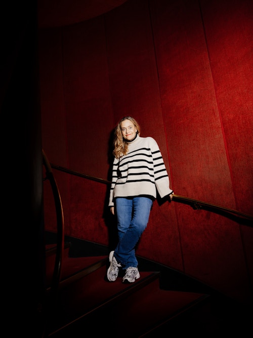 Foto av Henriette Steenstrup i trappen, hun har på seg en hvitstripet genser og blå olabukse.