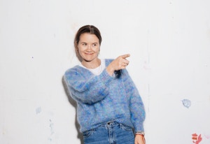 Høydebilde av Live Nelvik foran en vegg med noen malingsflekker, hvor hun peker på noe ute av bildet.