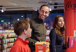 En mann er på kino med barna sine. En gutt og en jente holder i hver sin popcorn. Alle tre smiler og ser forventningsfulle ut.