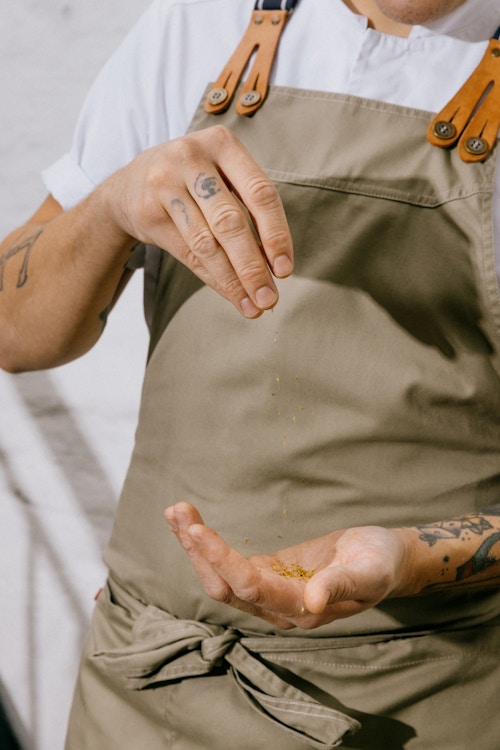 Bildet viser en person med forkle som drysser krydder mellom hendene.