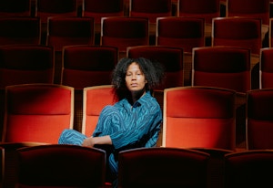 Mimmi Tamba sitter i en rød stol i salen der hun spiller teater