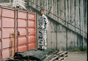 Portrett av rapperen Rambow som står på noen paller foran en container.