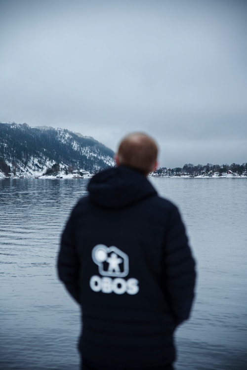 Et bilde av ryggen til Geir hvor det er en stor OBOS-logo på jakka.