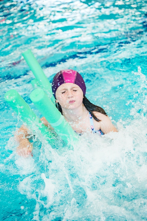Ei jente i bassenget med flytepinner for å holde seg over vann.