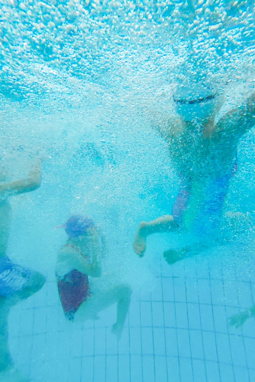 Foto tatt under vann av barna som svømmer rundt både over og under vann.