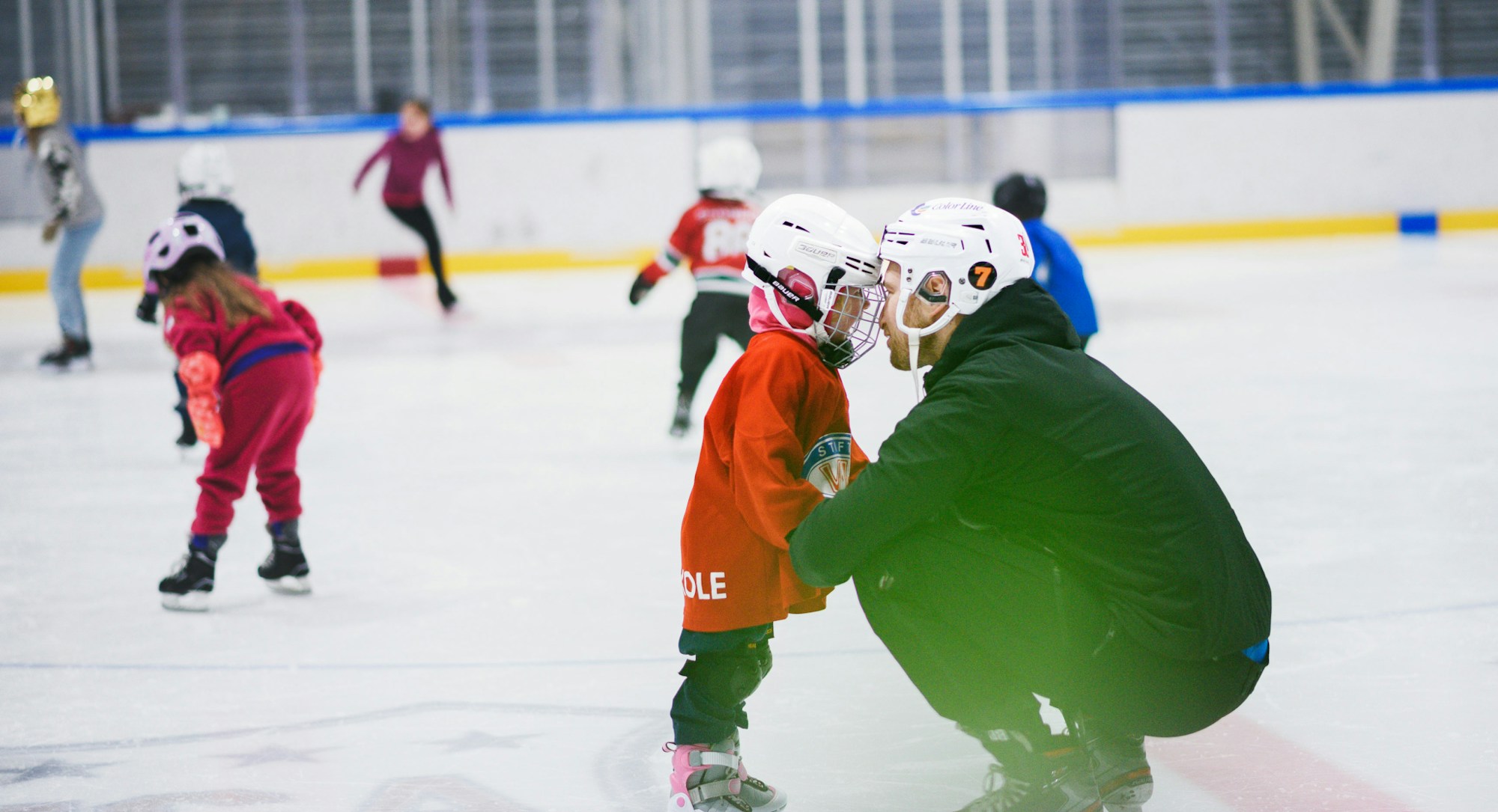 Foto av et barn med hockeyutstyr står på isen mens han lener ansiktet inn mot skøytetreneren og ser han inn i øynene.