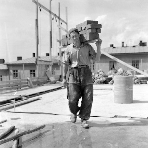 Historisk bilde av tømrer som bærer planker