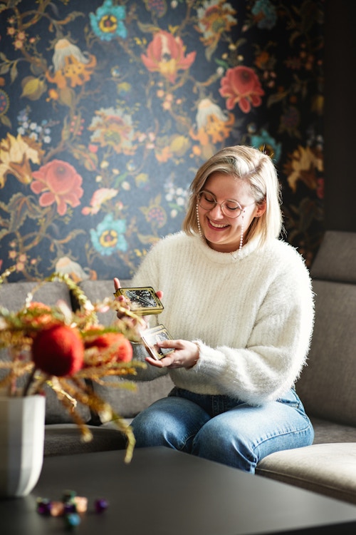 Foto av Kristine med Tarot-kort i hendene, sittende i sofaen i leiligheten sin på Firenga på Vear