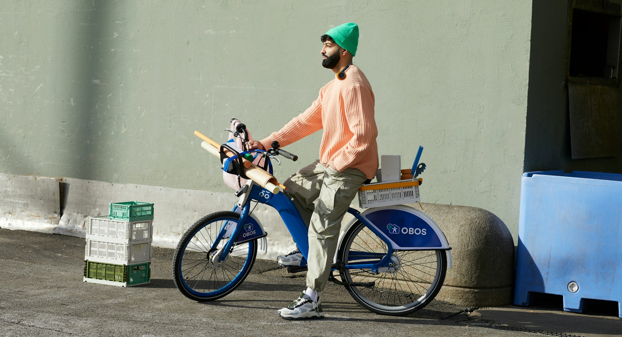 En mann på en bysykkel med fargerike klær. Sykkelen er lastet med ulike interiørting og ruller med papir.