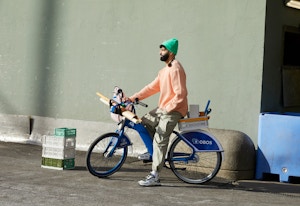 En mann på en bysykkel med fargerike klær. Sykkelen er lastet med ulike interiørting og ruller med papir.