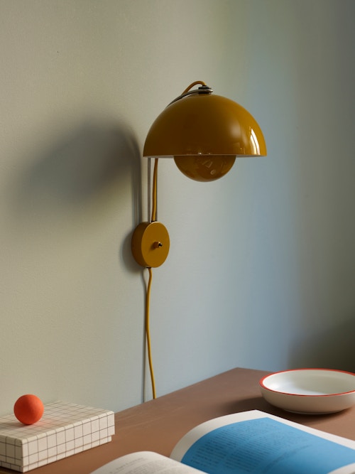 En gul lampe på en vegg over et skrivebord med ulike skrivebordsartikler som eske og bok.