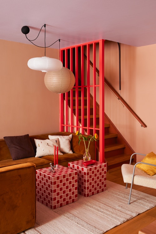 Bilde av sofakroken i leiligheten til Elena. Her ser vi den røde spileveggen, flisebordene, sofaen og ferskenfargen på veggen.