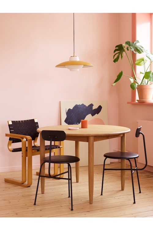 Rundt spisebord i tre med tre svarte stoler og en gul lampe i et rosa rom.