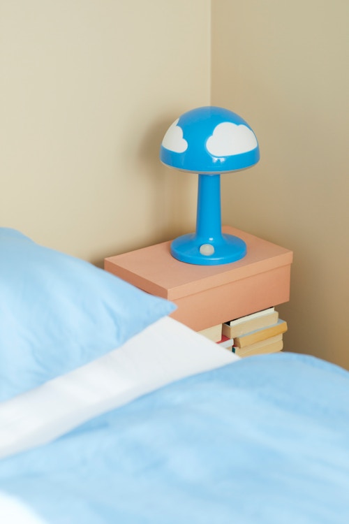 Utsnitt av seng og nattbord, med lyseblått sengesett og en blå lampe med små skyer på.