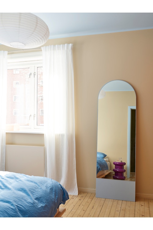 Soverommet med utsnitt av med sengen, vindu med gardiner foran og speil.