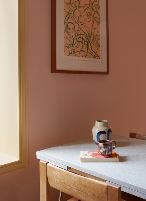 Kjøkkenbord foran en rosa vegg. På bordet er det en vase, en kopp og en bok.