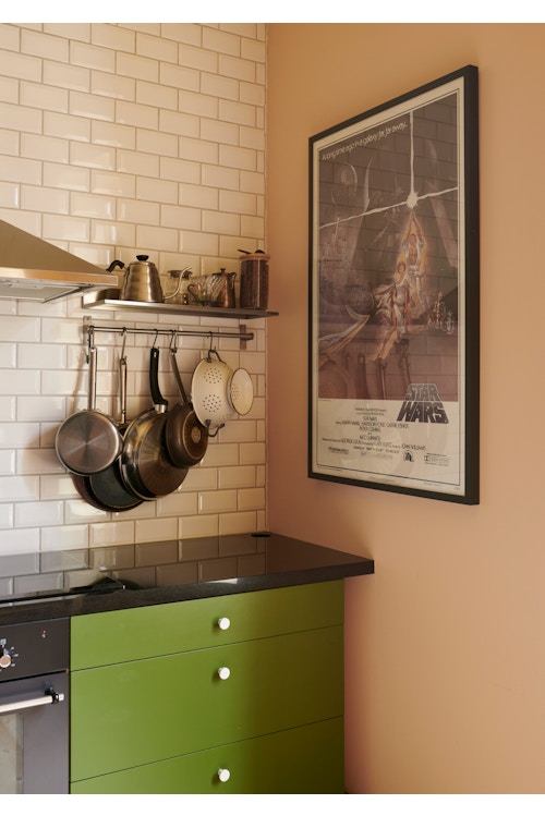 Grønne kjøkkenfronter og kjøkkenutstyr som henger på en vegg med hvite fliser over kjøkkenbenken.