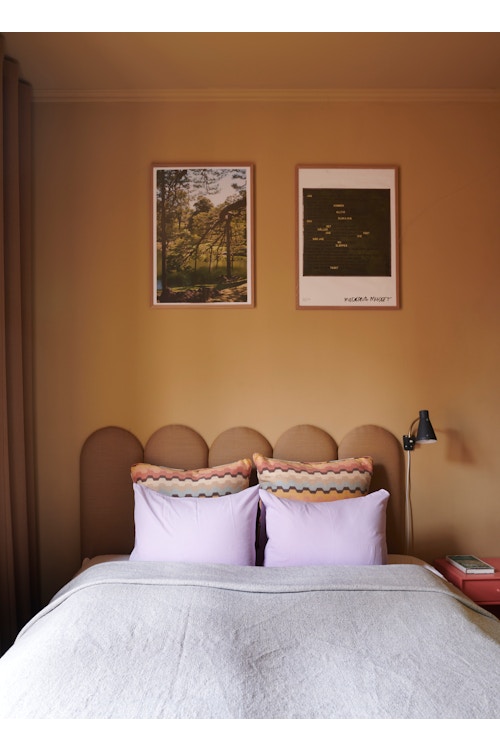 Oppredd seng med sengegavl. To bilder på en vegg malt i en varm terrakottatone.
