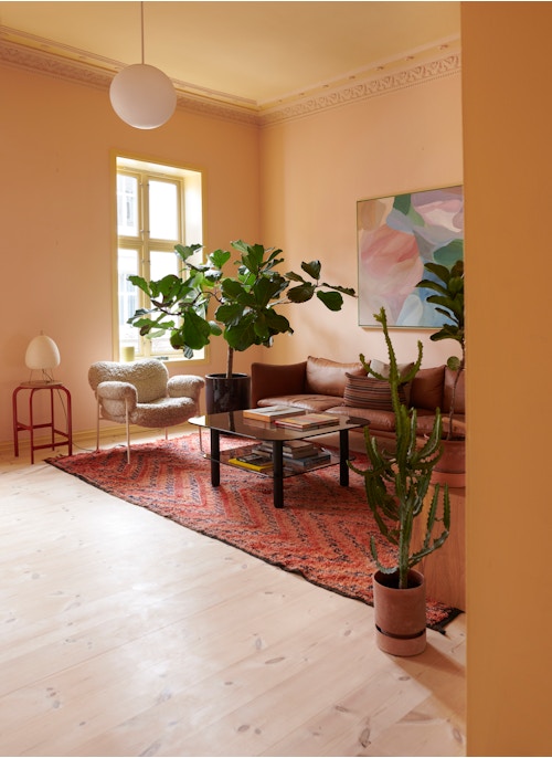 Stue malt i en dus, rosa farge. En kaktus står i forgrunnen og bak ser vi ulike stue møbler, belysning, planter og et vindu.