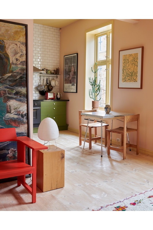 Grønt kjøkken med spisebord inntil en rosa vegg. Rød stol og et bilde i forgrunnen til venstre.
