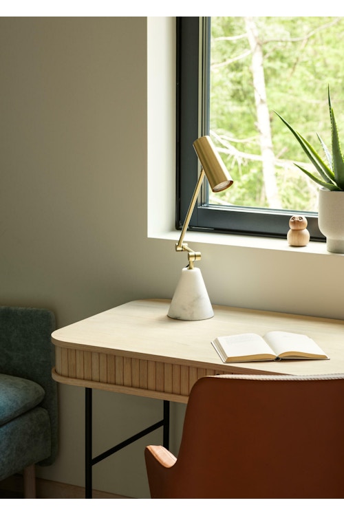 Skrivebord i eik, stol i skinn og en grå sofa på et kontor med utsikt ut over skogen
