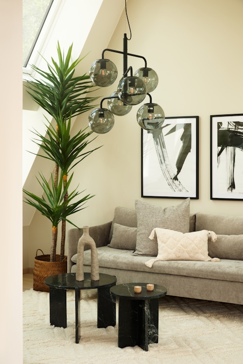 Beigemalt loftstue møblert med grå sofa, sofabord og grønne planter