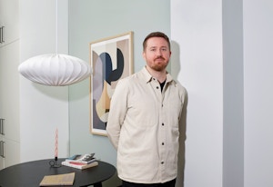 Portrett av Morten hjemme på kjøkkenet sitt med spisebord, lampe og bilde i bakgrunnen.