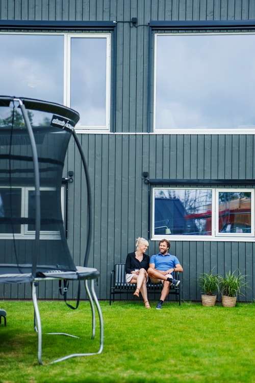 Susanne og Håvard sitter på en benk i hagen sin, med en trampoline i forgrunnen.