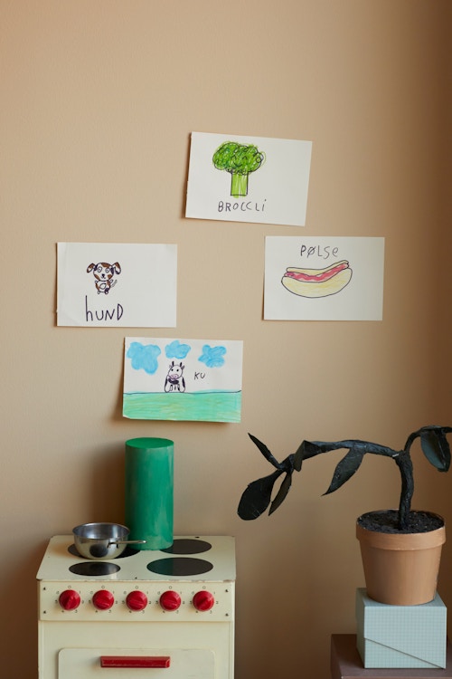 Detaljbilde av ferskenfarget vegg med barnetegninger pa og liten lekekomfyr foran