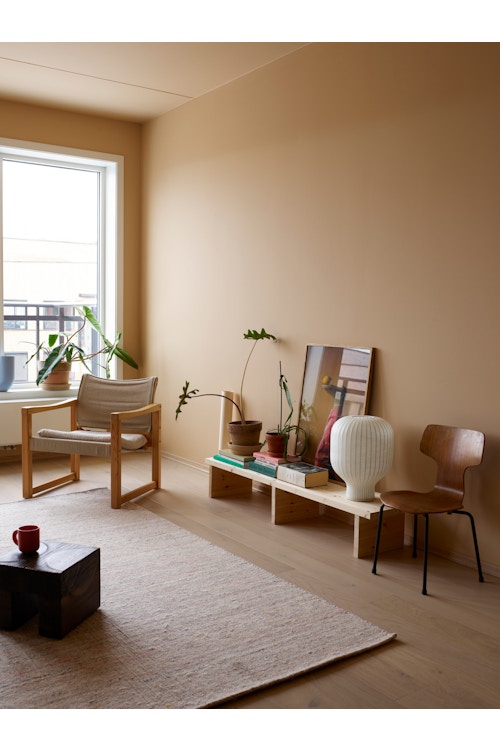 Ferskenfarget stue med lenestol i tre, beige gulvteppe og lav skjenk med pyntegjenstander.