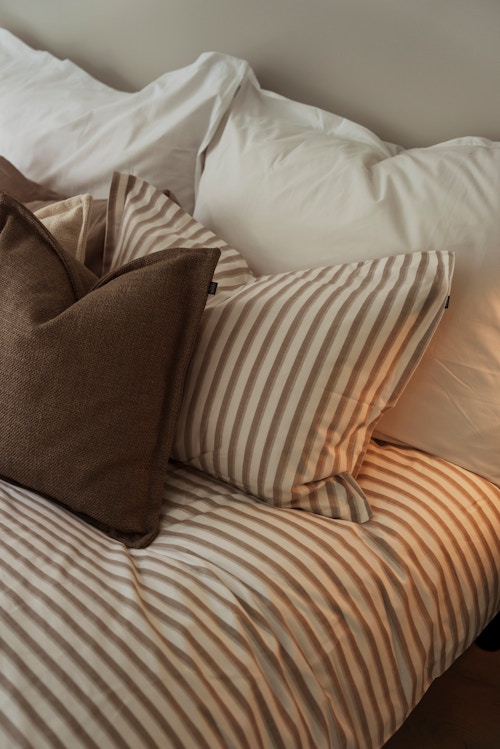 Nærbilde av en seng med dyne og puter i forskjellige størrelse og farger i MIDT.