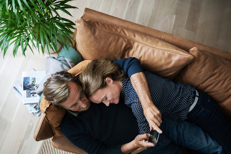 Mann og dame ligger på sofaen og ser på mobilen som mannen holder.