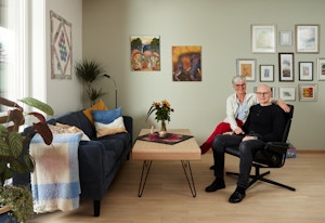Foto av Solveig og Per som sitter i stua i leiligheten sin, med mange bilder på veggene.