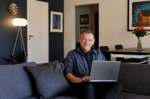 Styreleder Jorulf Breitland sitter i sofaen i hjemmet sitt med PC-en i fanget.